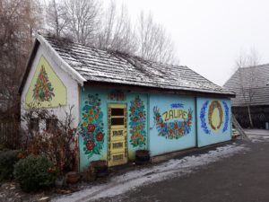 a small building in Zalipie, Poland decorated with floral paintings with a little snow on the wooden shingle roof