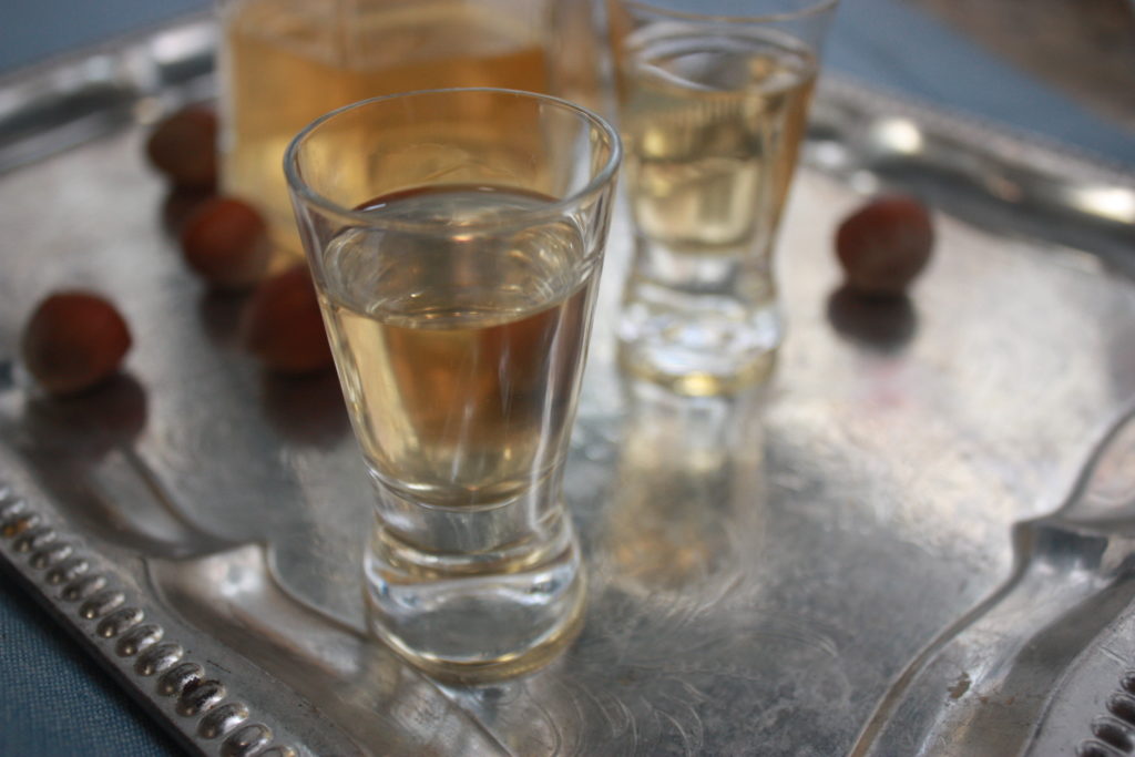 hazelnut liqueur in shot glasses on a silver tray with whole hazelnuts and a bottle in the background