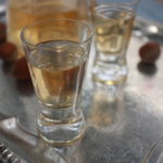 hazelnut liqueur in shot glasses on a silver tray with whole hazelnuts and a bottle in the background