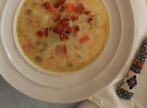 Polish potato soup in a white bowl topped with crumbled bacon
